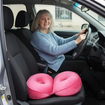 A woman smiling at the wheel of her car, her pink Seatzy cushion on the passenger seat beside her
